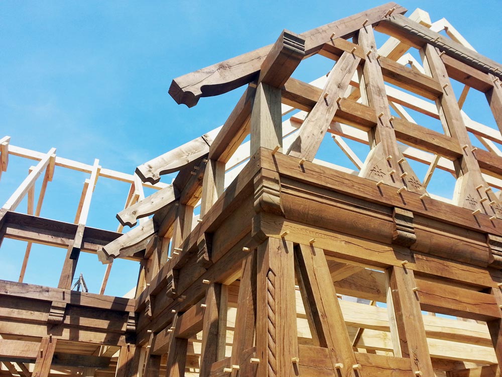 Nahaufnahme der kunstvollen, geschnitzten und verzierten Holzbalken eines Fachwerks, mit einem hellblauen Himmel im Hintergrund.